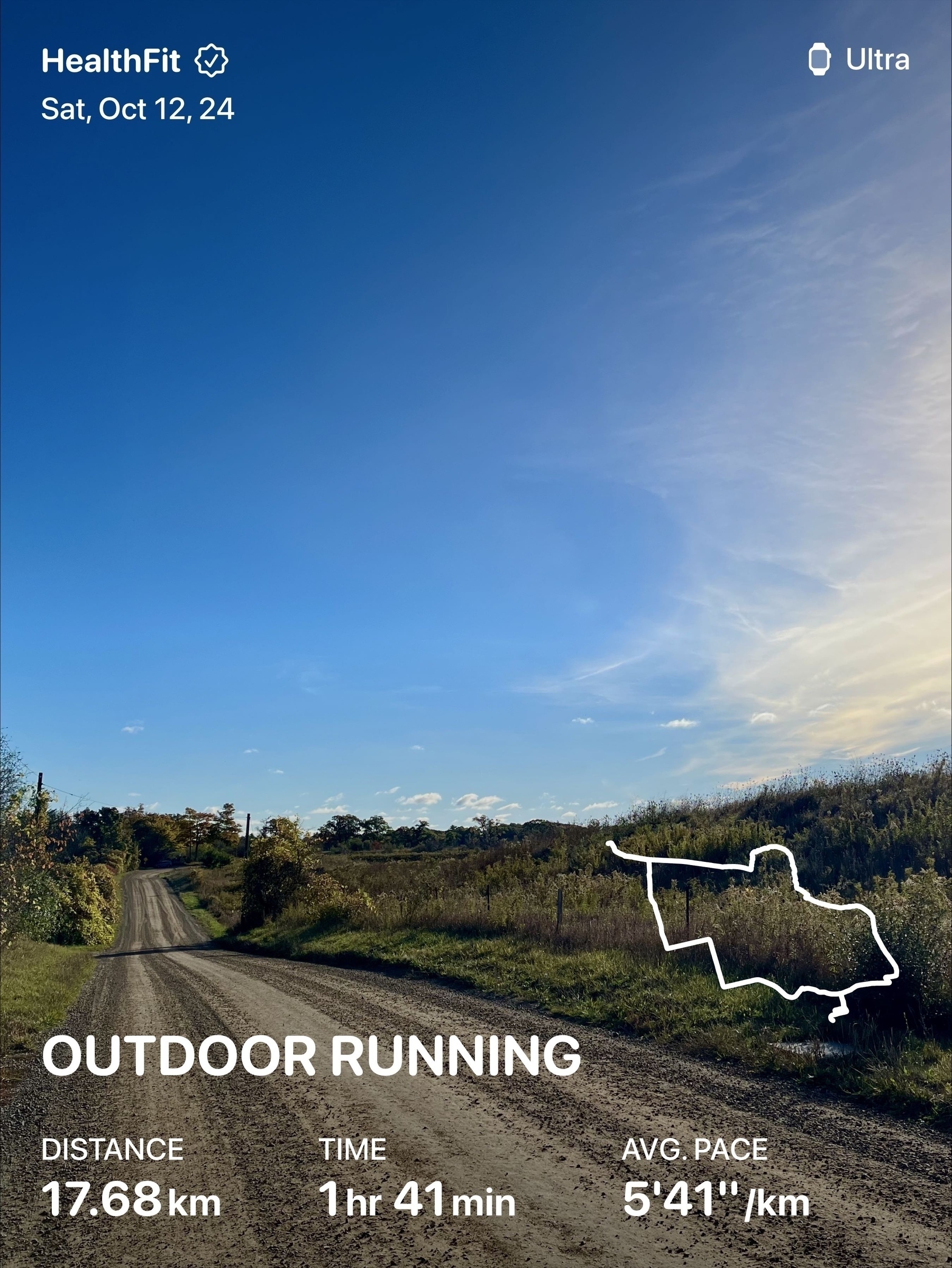 A dirt road runs through a countryside landscape under a clear blue sky, with overlayed information detailing an outdoor running activity of 17.68 km at an average pace of 5'41" per kilometer.